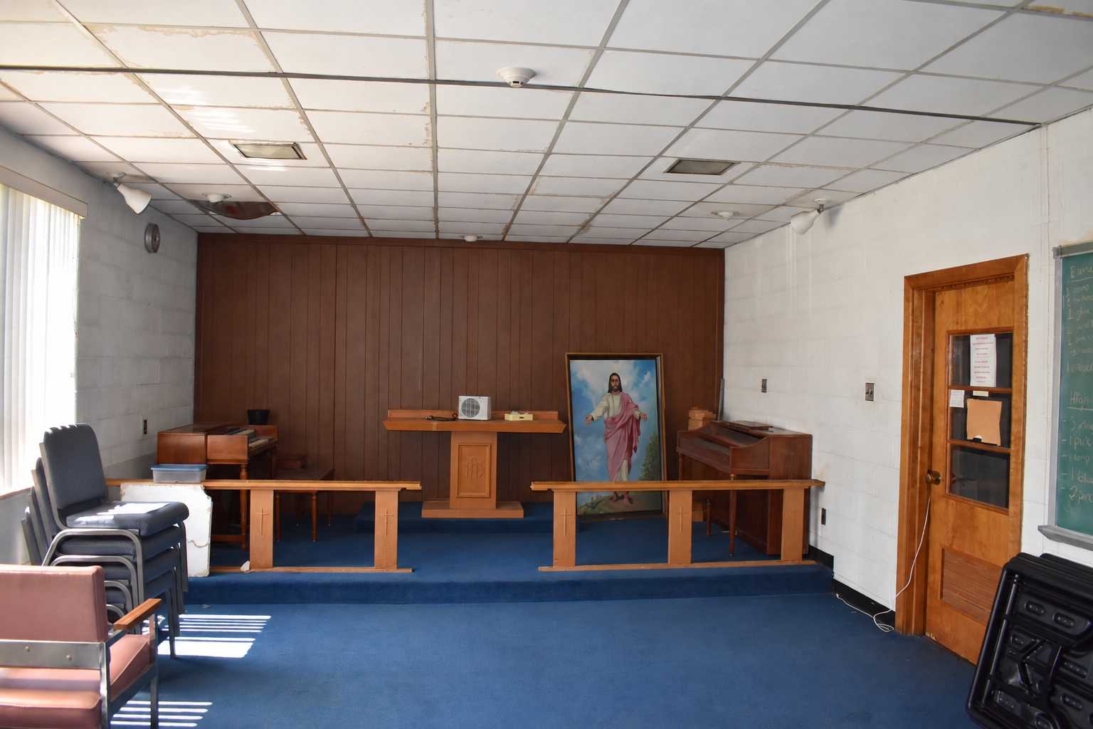 Chapel room before renovation, with blue carpeting, paneled backdrop and existing stage