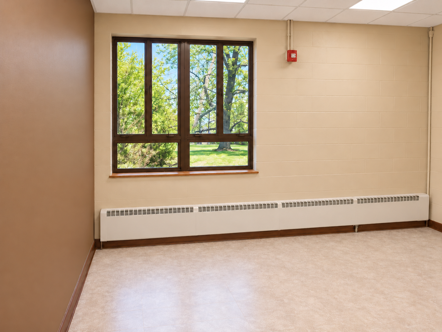 Classroom with a solid brown left accent wall, tan window wall, bronze window frames, wood-brown base trim, a long light radiator and light flooring