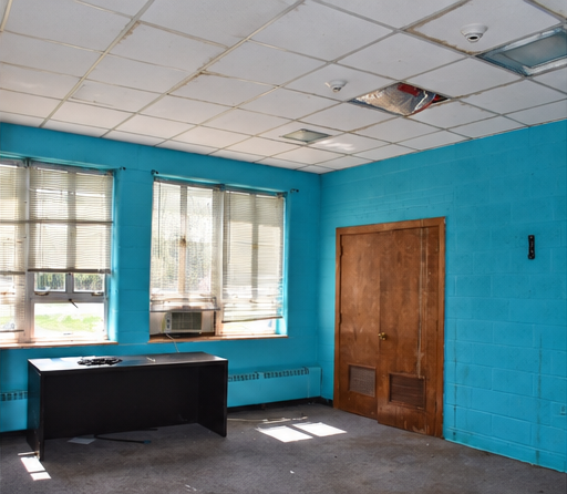 Blue-wall classroom with a desk, carpet, window blinds and brown closet doors