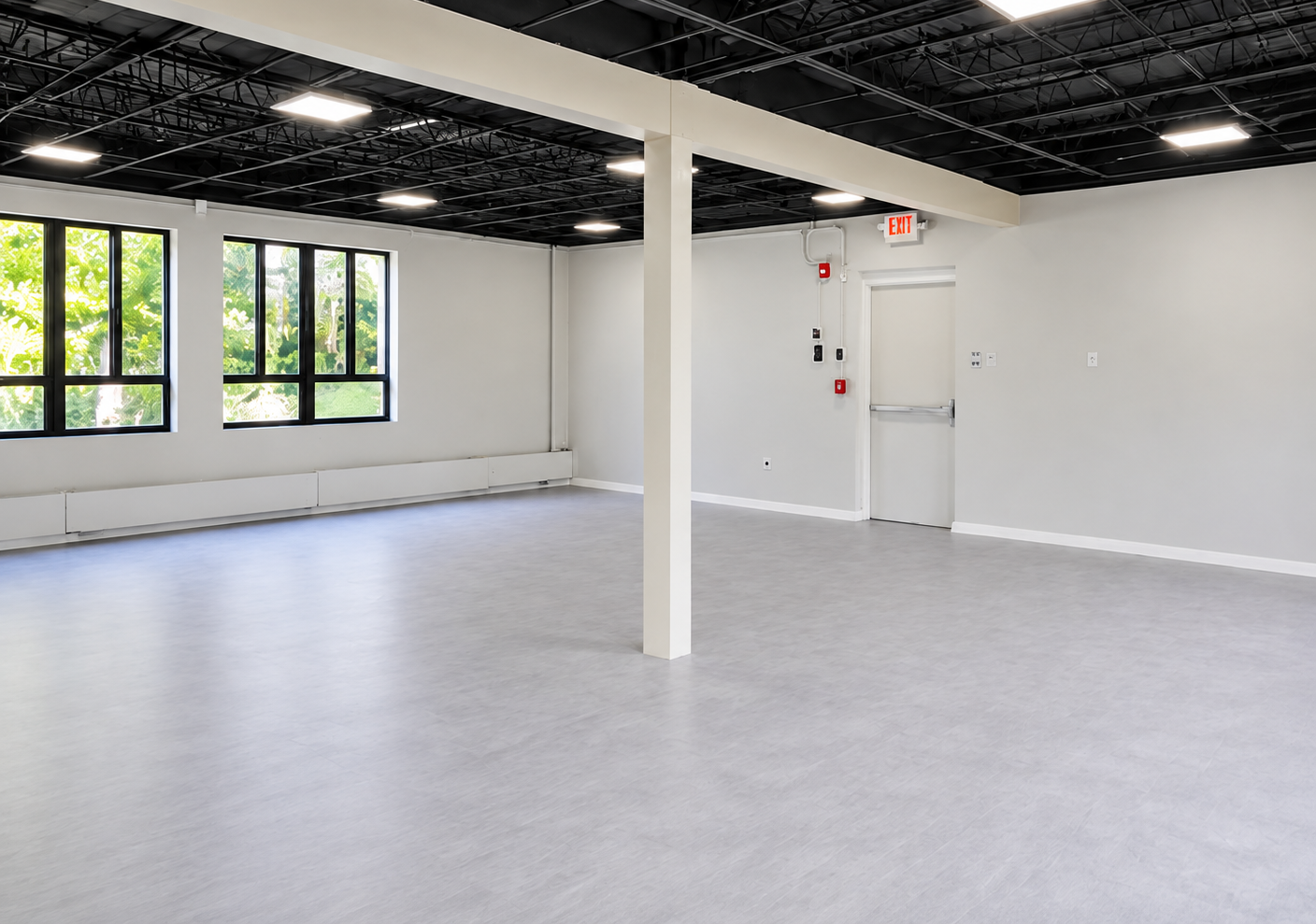 Daycare room with light flooring, exposed dark ceiling, windows and a central column