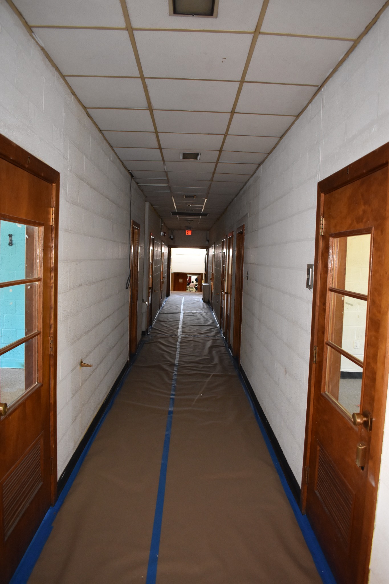 Alternate portrait hallway view with floor protection and existing ceiling panels before overhead work