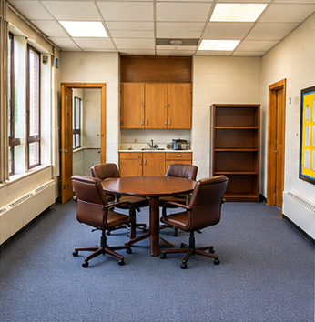 Carpeted meeting area with round table, chairs, wood cabinets, sink and shelving