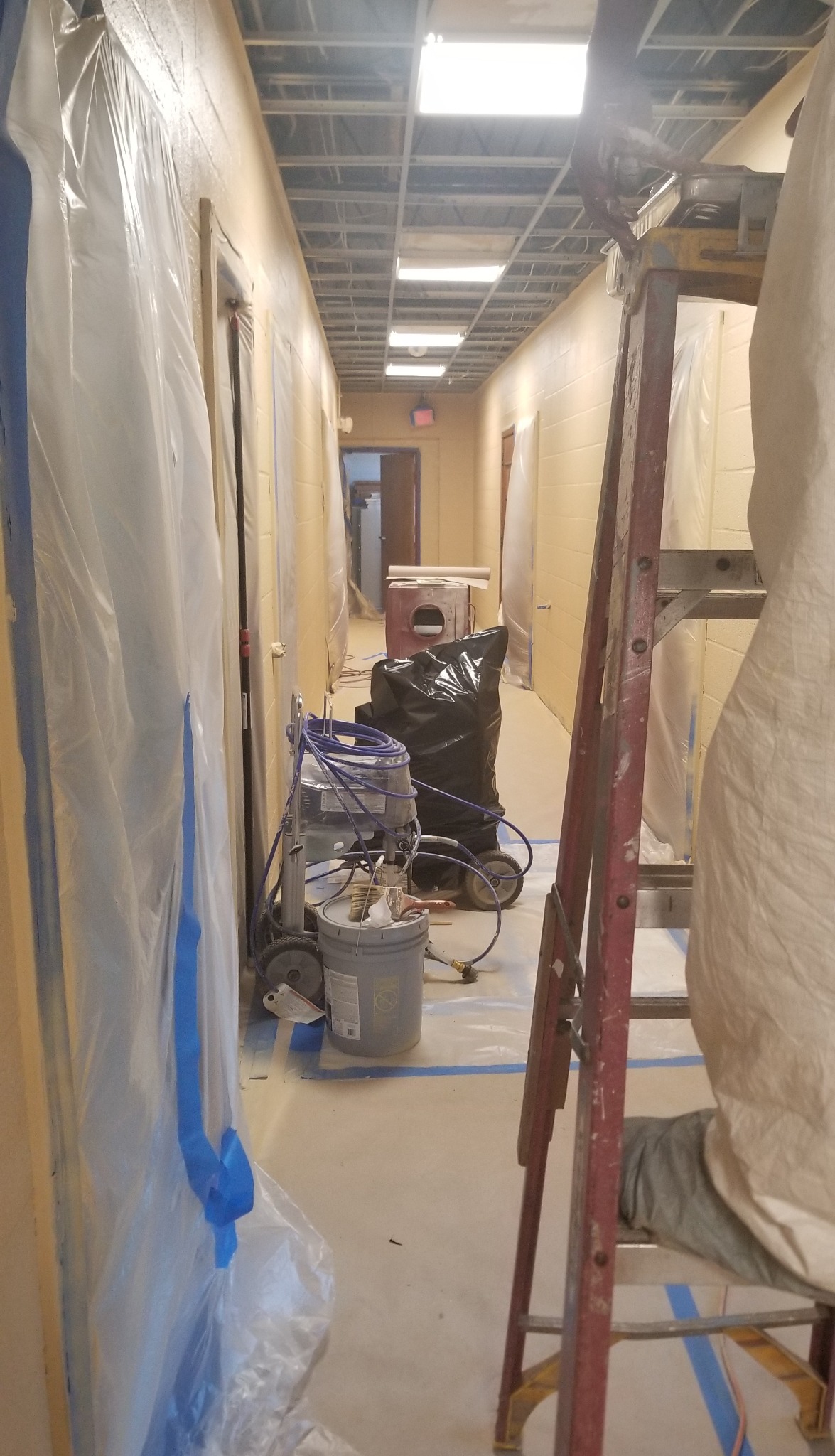 Hallway overhead and wall work with temporary protection, a ladder and equipment