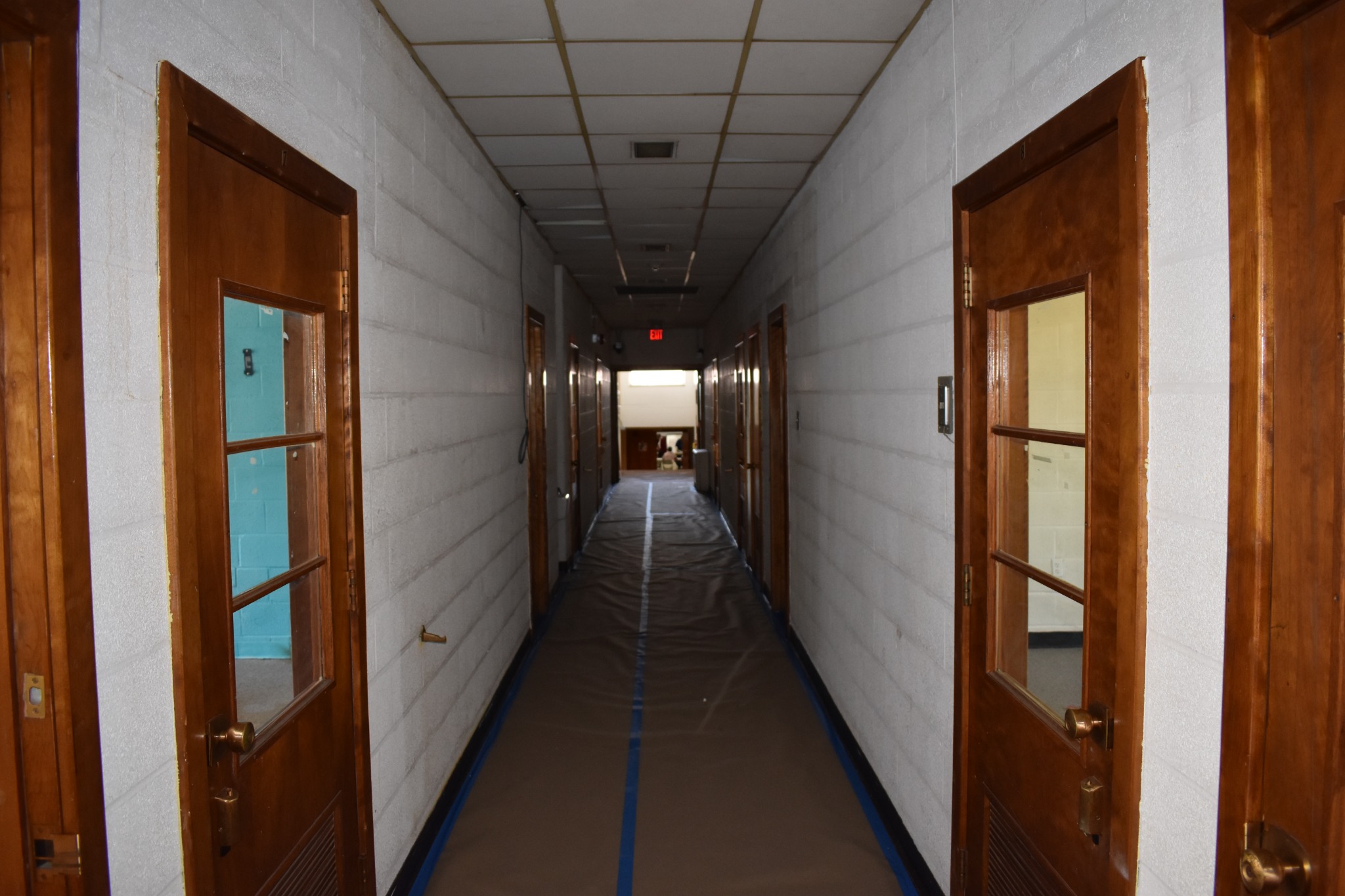 Hallway with existing ceiling panels and floor protection in place before overhead work