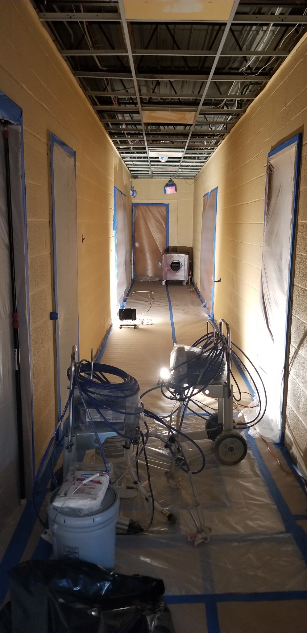 Hallway with ceiling panels removed, protected doorways and flooring, sprayers and hoses