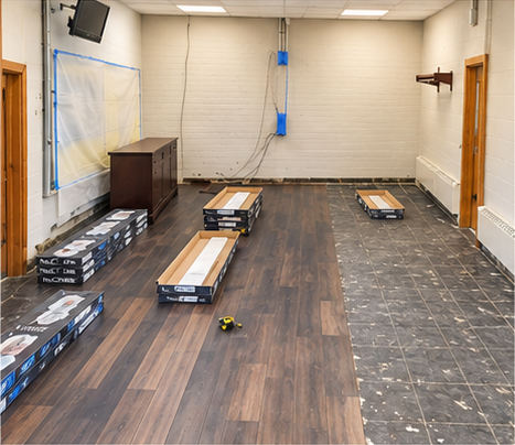 Partially installed brown wood-look planks beside exposed dark flooring, with open boxes and tools
