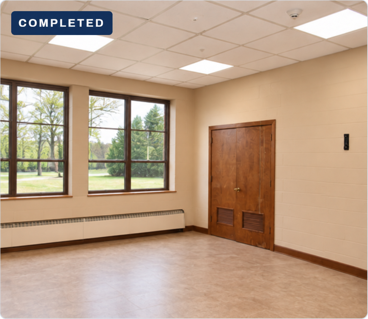 Tan-wall classroom with clear windows, light flooring and closed brown closet doors, without a desk