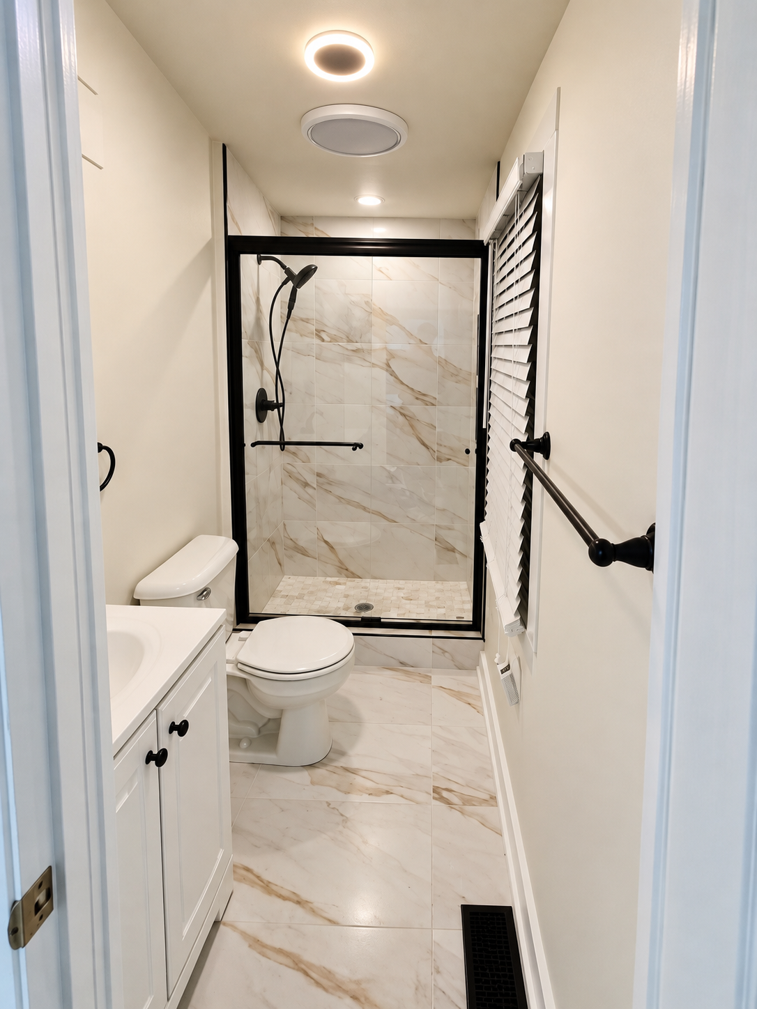 Bright finished bathroom presentation with a black-framed glass shower enclosure, black fixtures, white vanity, toilet and marble-look flooring.