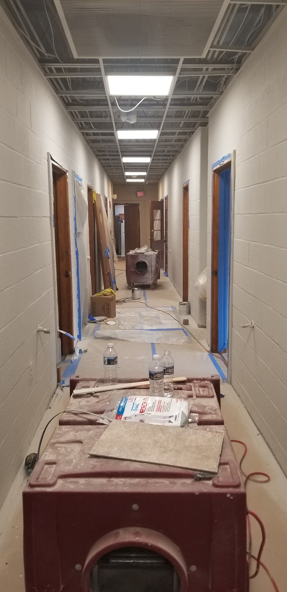 Later-stage hallway wall and lighting work with floor protection and equipment still in place