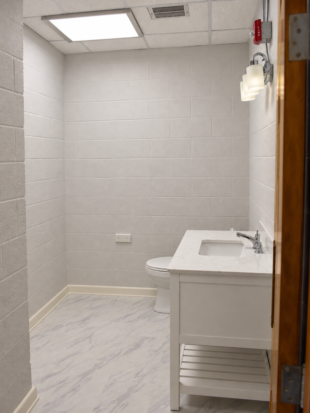 Bathroom doorway view with white vanity on the right, light walls, ceiling light and grille, and white-and-gray marble-look floor